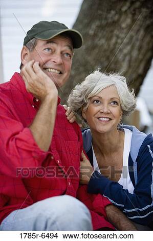 Picture - Mature couple in work clothes sitting outside and looking up. Fotosearch