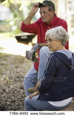 Stock Image - Mature couple in work clothes sitting outside. Fotosearch