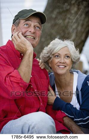 Stock Photography - Mature couple in work clothes sitting outside and looking up. Fotosearch