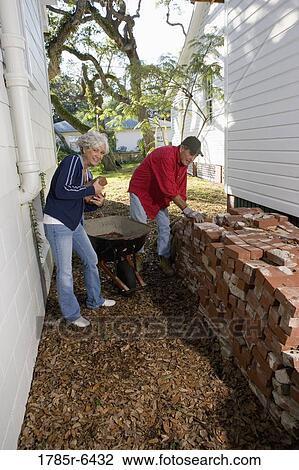 Mature couple loading bricks on wheelbarrow outside house View Large Photo Image Stock Image - Mature couple loading bricks on wheelbarrow outside house. Fotosearch