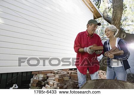 Mature couple loading bricks on wheelbarrow outside house View Large Photo Image Stock Image - Mature couple loading bricks on wheelbarrow outside house. Fotosearch