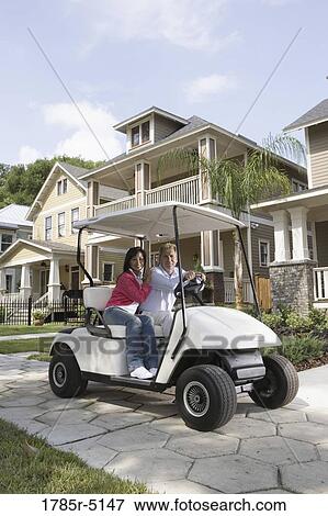 Stock Photo - Mature couple riding golf cart through the neighborhood. Fotosearch