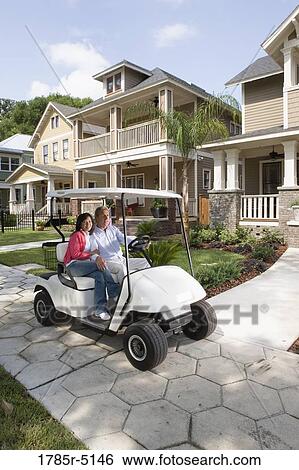 Stock Photograph - Mature couple riding golf cart through the neighborhood. Fotosearch
