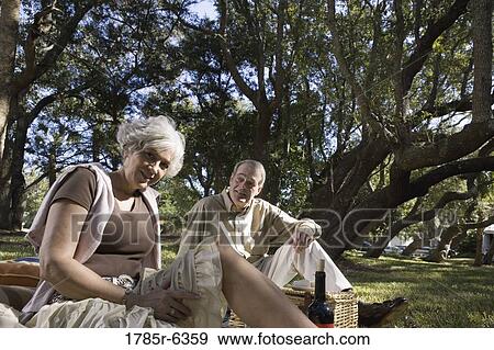 Stock Photo - Mature couple sitting on a picnic blanket in a park. Fotosearch