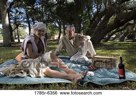 Mature couple sitting on a picnic blanket in a park View Large Photo Image Stock Photograph - Mature couple sitting on a picnic blanket in a park. Fotosearch