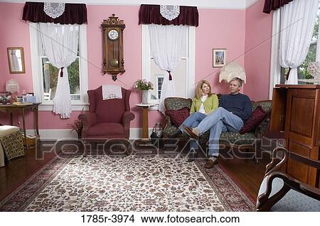 Mature couple sitting on a sofa in living room View Large Photo Image Picture - Mature couple sitting on a sofa in living room. Fotosearch