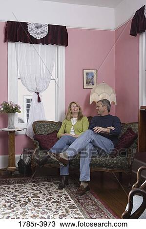 Mature couple sitting on a sofa in living room View Large Photo Image Stock Image - Mature couple sitting on a sofa in living room. Fotosearch