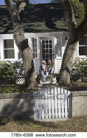 Stock Photo - Mature couple sitting on front steps of a house surrounded by tall oak trees. Fotosearch