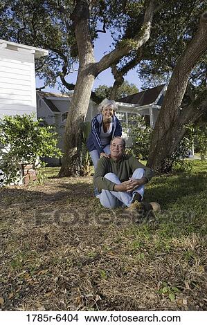 Mature couple sitting on front yard of house, surrounded by tall oak trees View Large Photo Image Picture - Mature couple sitting on front yard of house, surrounded by tall oak trees. Fotosearch