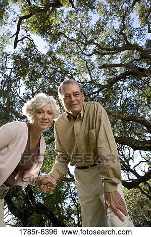 Stock Photograph - Mature couple standing together under oak trees. Fotosearch