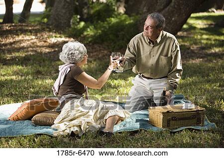 Stock Image - Mature couple toasting with wine glasses at a picnic in the park. Fotosearch