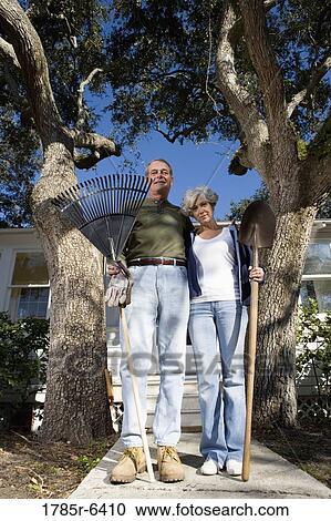 Mature couple with gardening tools in front of house surrounded by tall oak trees View Large Photo Image Stock Image - Mature couple with gardening tools in front of house surrounded by tall oak trees. Fotosearch