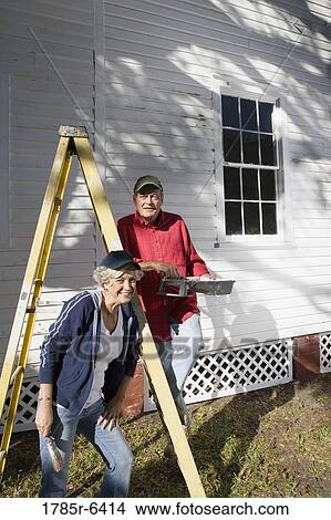 Mature couple with ladder and painting tools preparing to paint outside of house View Large Photo Image Picture - Mature couple with ladder and painting tools preparing to paint outside of house. Fotosearch