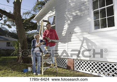 Picture - Mature couple with ladder and painting tools preparing to paint outside of house. Fotosearch