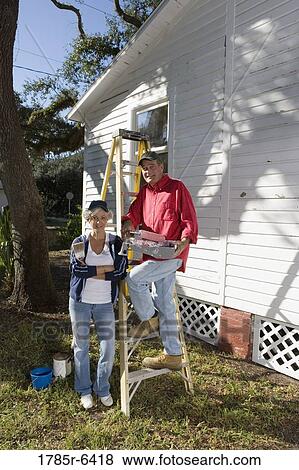 Stock Photo - Mature couple with ladder and painting tools preparing to paint outside of house. Fotosearch