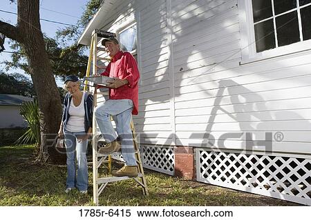 Stock Photography - Mature couple with ladder and painting tools preparing to paint outside of house. Fotosearch