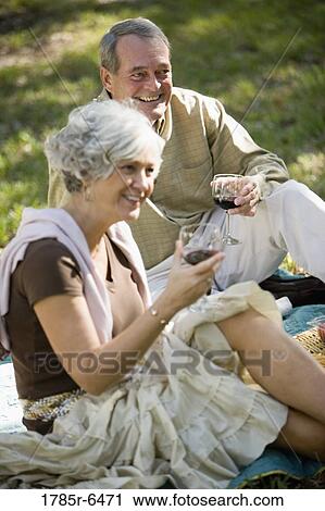 Stock Image - Mature couple with wine glasses sitting on a blanket on the grass. Fotosearch