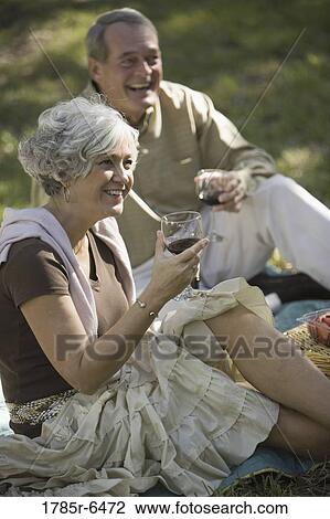 Mature couple with wine glasses sitting on a blanket on the grass View Large Photo Image Stock Image - Mature couple with wine glasses sitting on a blanket on the grass. Fotosearch