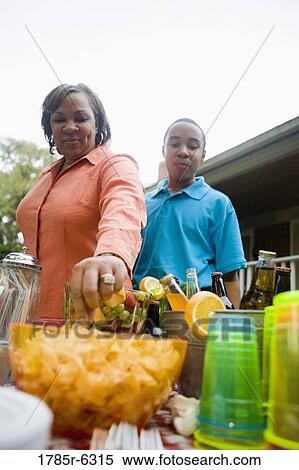 Stock Photography - Mature woman standing with her son by picnic table having snack. Fotosearch