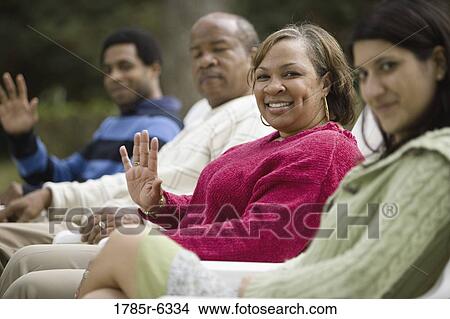 Mature woman waving with family in background View Large Photo Image Picture - Mature woman waving with family in background. Fotosearch