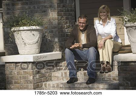 Stock Image - Mid adult couple sitting on front steps of house. Fotosearch