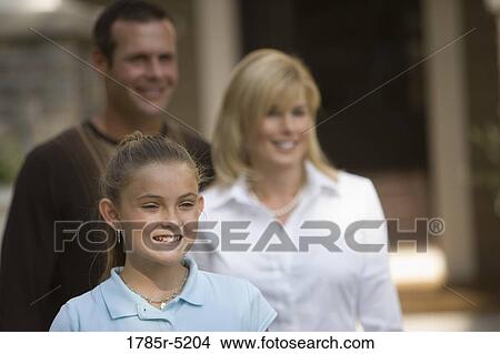 Mid adult couple standing with their daughter in front of their house View Large Photo Image Picture - Mid adult couple standing with their daughter in front of their house. Fotosearch