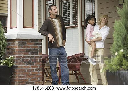 Stock Photo - Mid adult couple with young child standing outside a house. Fotosearch