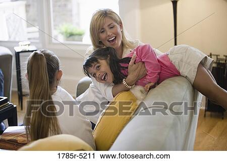 Mother playing with her daughters on a sofa in living room View Large Photo Image Stock Image - Mother playing with her daughters on a sofa in living room. Fotosearch