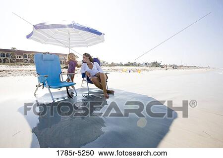 Mother sitting on beach chair under a beach umbrella, looking at her young daughter View Large Photo Image Stock Image - Mother sitting on beach chair under a beach umbrella, looking at her young daughter. Fotosearch