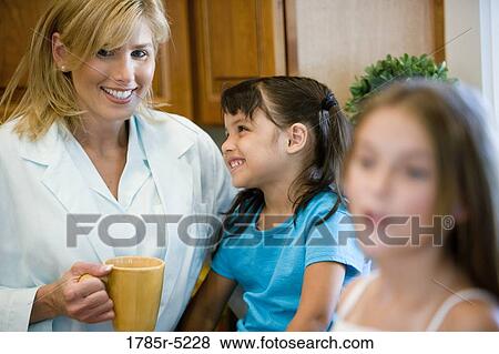 Stock Photo - Mother standing with daughters in the kitchen. Fotosearch
