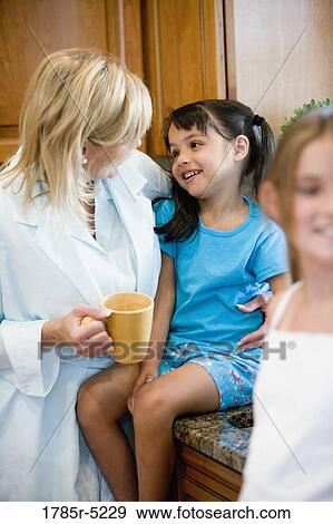 Stock Photo - Mother standing with daughters in the kitchen. Fotosearch