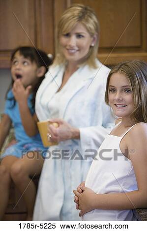 Stock Photography - Mother standing with daughters in the kitchen. Fotosearch