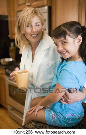 Stock Photograph - Mother with her playful daughter sitting on the kitchen counter. Fotosearch