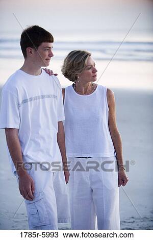 Stock Image - Mother with teenage son on beach looking away. Fotosearch