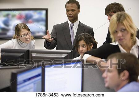Stock Image - Office workers gathered around computer screens. Fotosearch