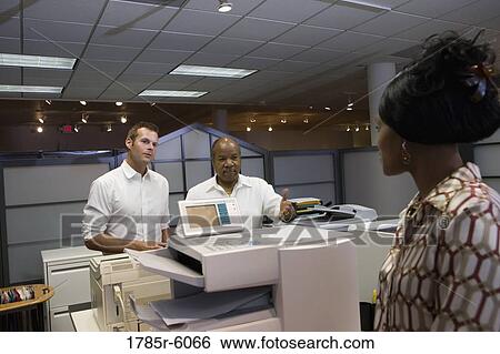 Stock Photograph - Office workers talking by photocopier. Fotosearch