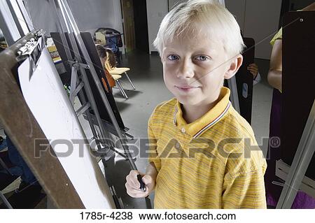 Portrait of a boy standing by a drawing easel in art class View Large Photo Image Stock Photo - Portrait of a boy standing by a drawing easel in art class. Fotosearch
