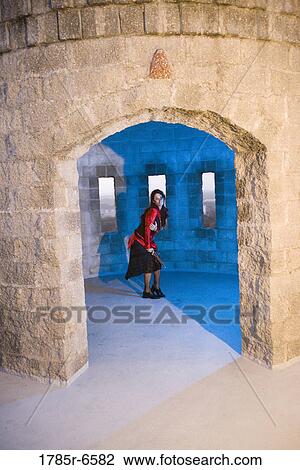 Stock Image - Portrait of a frightened woman pirate armed with a gun standing inside a castle turret. Fotosearch