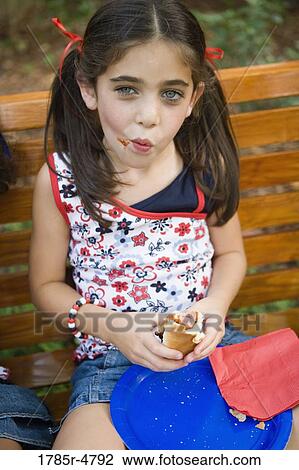 Portrait of a girl sitting on a bench eating a hotdog View Large Photo Image Stock Image - Portrait of a girl sitting on a bench eating a hotdog. Fotosearch