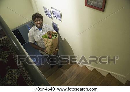 Portrait of a man climbing stairs holding a grocery bag filled with groceries View Large Photo Image Stock Image - Portrait of a man climbing stairs holding a grocery bag filled with groceries. Fotosearch