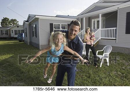 Stock Photograph - Portrait of a man playing with his blue-collar family in front of a trailer home. Fotosearch