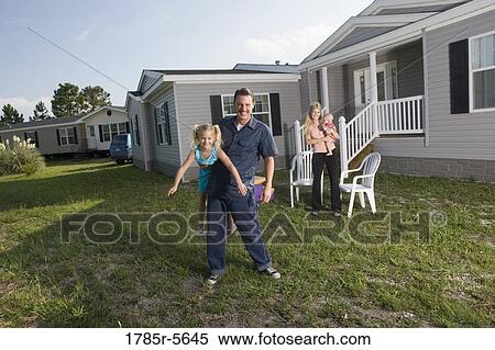 Stock Photography - Portrait of a man playing with his blue-collar family in front of a trailer home. Fotosearch