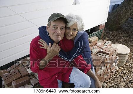 Portrait of a mature couple embracing while sitting on stack of bricks outside house View Large Photo Image Stock Image - Portrait of a mature couple embracing while sitting on stack of bricks outside house. Fotosearch