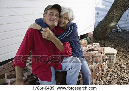 Portrait of a mature couple embracing while sitting on stack of bricks outside house View Large Photo Image Stock Photo - Portrait of a mature couple embracing while sitting on stack of bricks outside house. Fotosearch