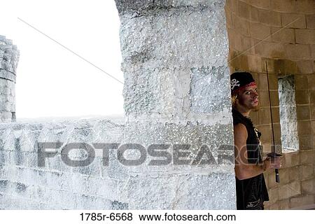Portrait of a pirate armed with a sword leaning and hiding against a castle wall View Large Photo Image Stock Photo - Portrait of a pirate armed with a sword leaning and hiding against a castle wall. Fotosearch