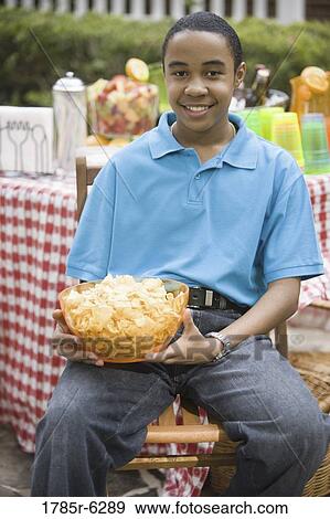 Portrait of a seated teenage boy holding a bowl of snacks View Large Photo Image Stock Photo - Portrait of a seated teenage boy holding a bowl of snacks. Fotosearch