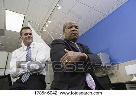 Portrait of a serious manager thinking while younger office worker smiles behind View Large Photo Image Stock Image - Portrait of a serious manager thinking while younger office worker smiles behind. Fotosearch