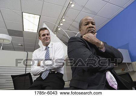 Portrait of a serious manager thinking while younger office worker smiles behind View Large Photo Image Stock Image - Portrait of a serious manager thinking while younger office worker smiles behind. Fotosearch