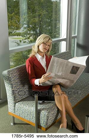 Stock Photography - Portrait of a smiling businesswoman sitting in a lobby reading a newspaper. Fotosearch