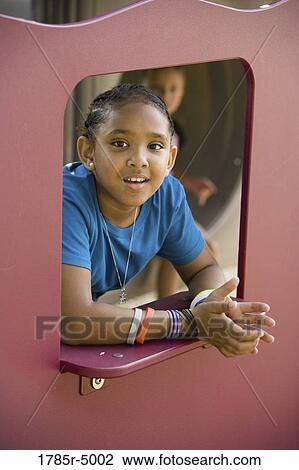 Portrait of a smiling girl looking through an opening at a playground View Large Photo Image Stock Image - Portrait of a smiling girl looking through an opening at a playground. Fotosearch